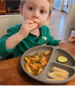 Little boy in green shirt eating cucumber slice from plate of food